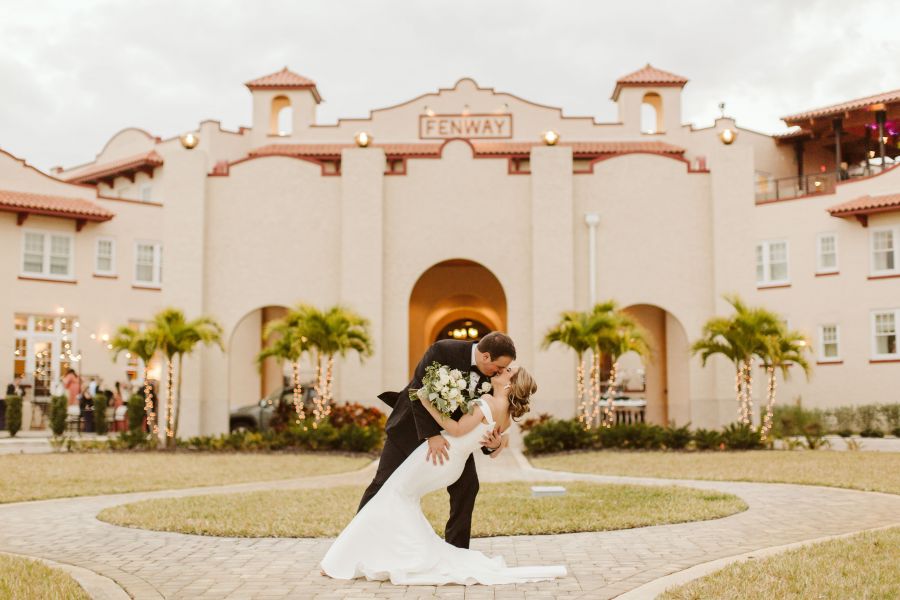 A person in a suit and person in a wedding dress kissing in front of a building in Dunedin FL