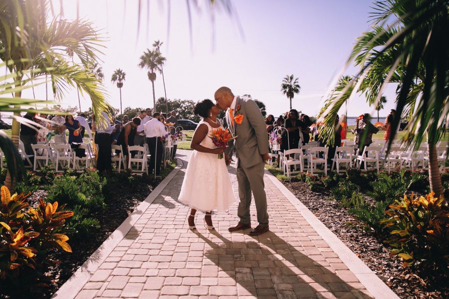 A person in a wedding dress and person in a suit kissing on a path of Fenway Hotel