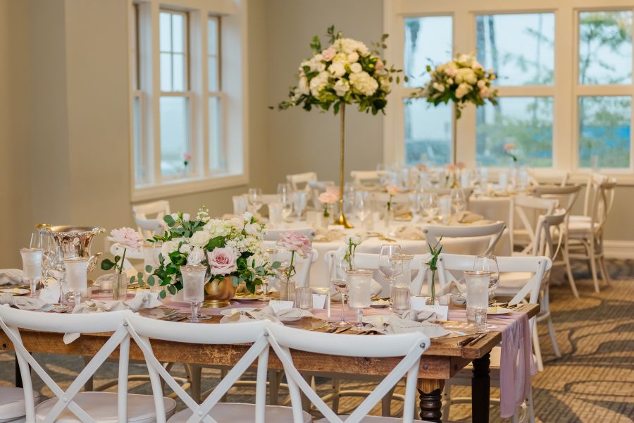 A room with tables and chairs with flower and glasses as decorations