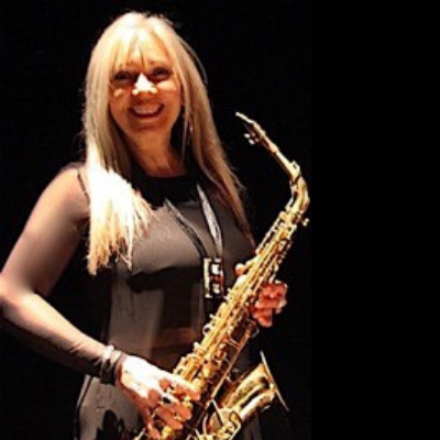 A person smiling for a photo on a stage holding a saxophone under a spotlight